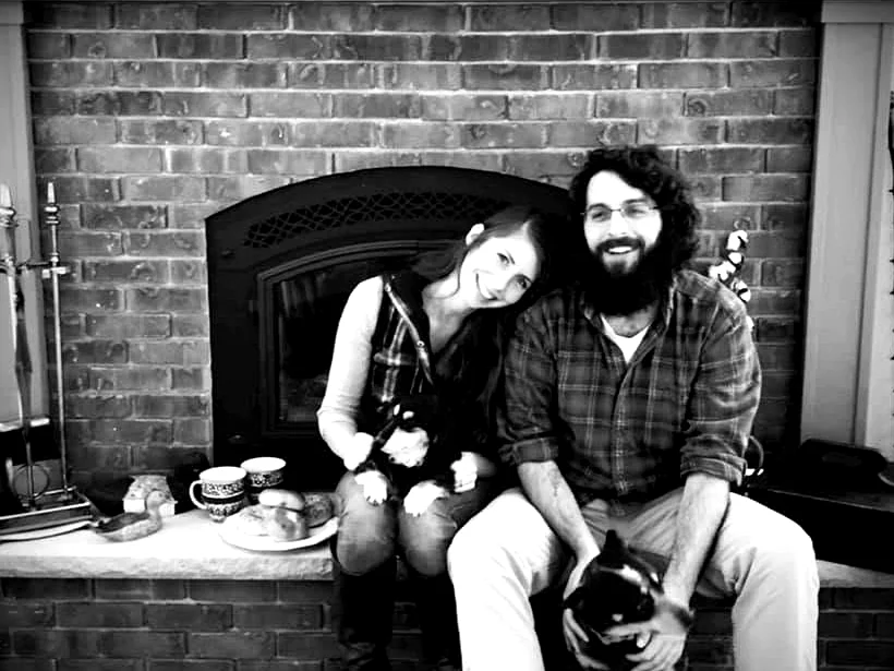 The people behind Wild Ember Engraving sitting by a fireplace with their dogs.